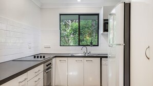 A modern kitchen with white cabinets, a black countertop, a window with a view of greenery, and a built-in microwave.