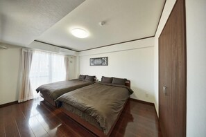 A bedroom with two beds, a ceiling light, a window with curtains, and a door.