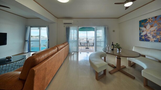 A modern living room with a sofa, a dining table, and a ceiling fan. - FreedomHills A (Tomigusuku)
