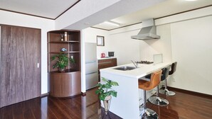 A modern kitchen with a central island, wooden shelving, and a built-in microwave. - FreedomHills A (Tomigusuku)