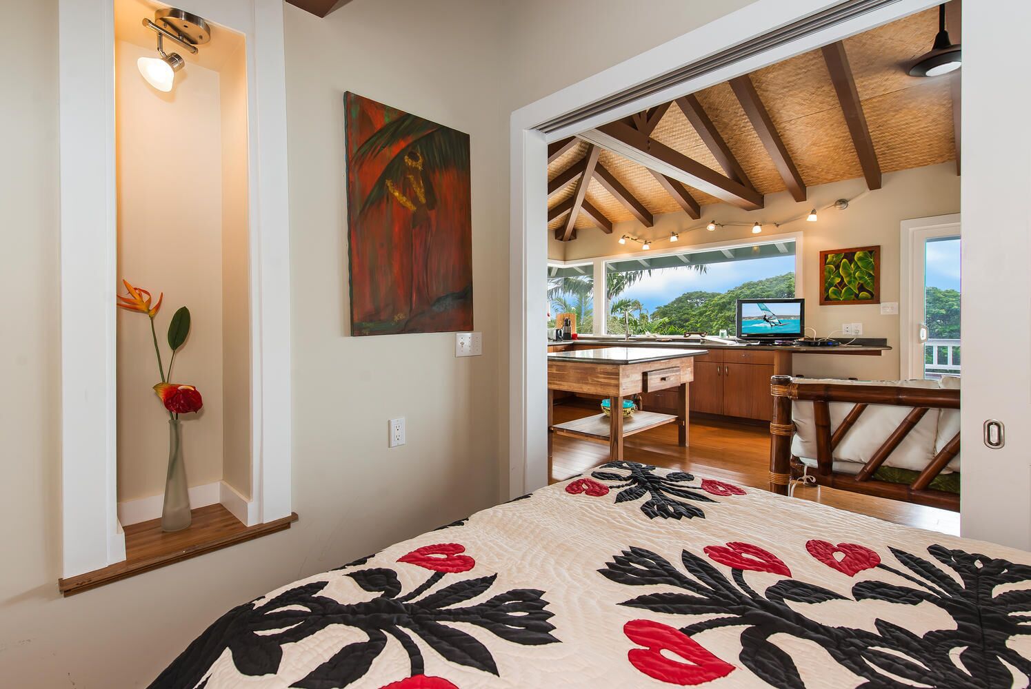 A bedroom with a bed, a painting, and a view of the outdoors.