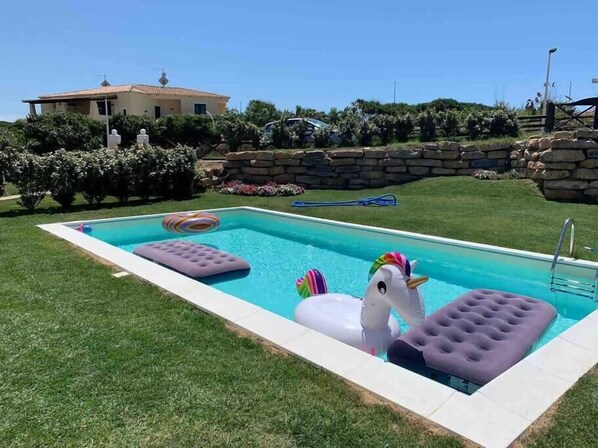 A rectangular swimming pool with a stone wall and a house in the background. - Villa Cristallina Private Pool, Wi-Fi & Netflix (Stintino)