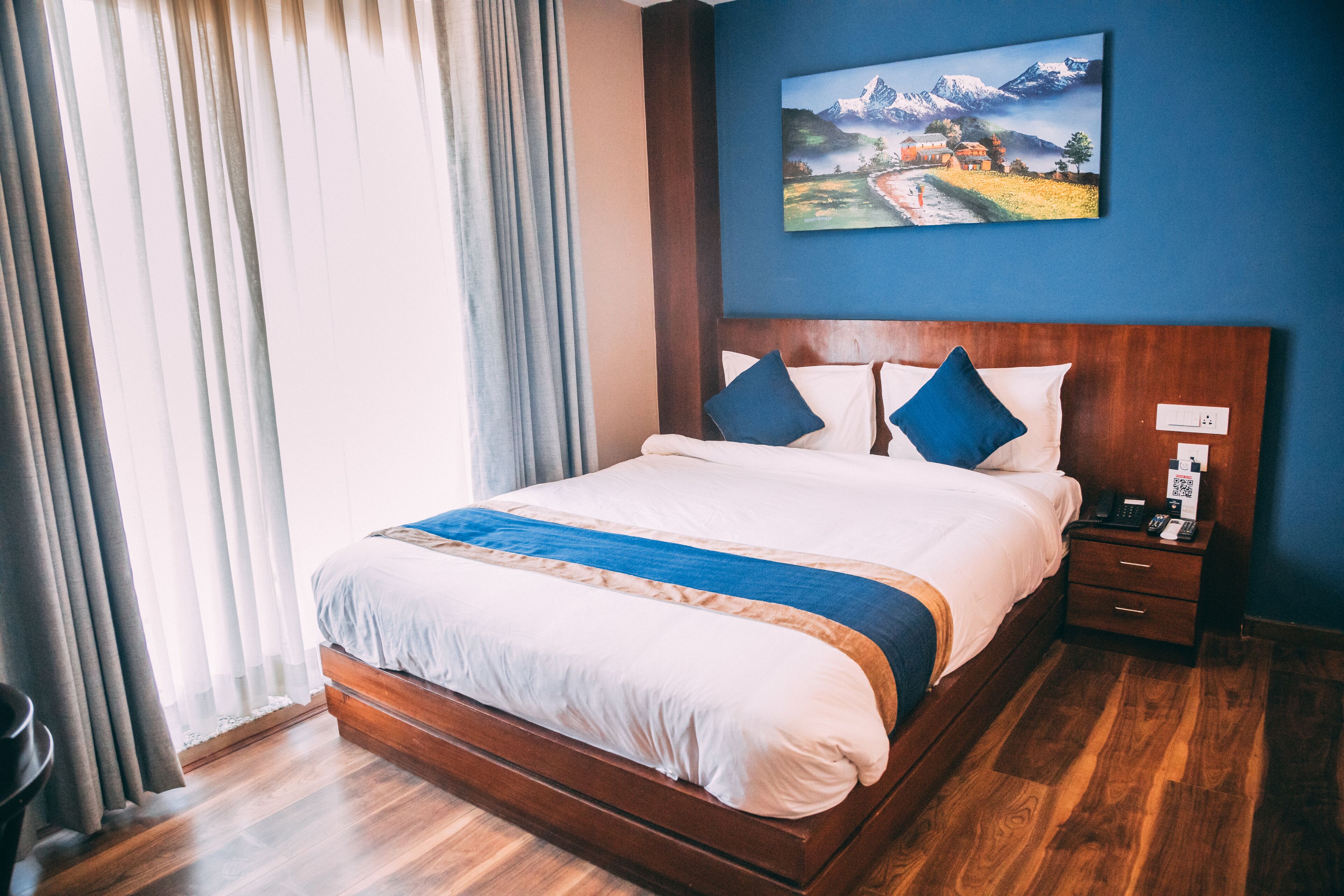 A large bed with a wooden frame, two pillows, and a bedside table with a phone and a lamp.