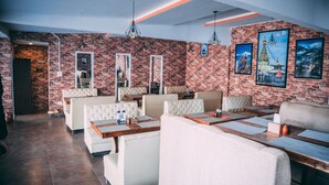 A restaurant with brick walls, white cushioned seating, and wooden tables. - Himalayan Suite Hotel (Kathmandu)
