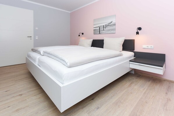 A modern bedroom with a white bed, a bedside table, and a wall-mounted lamp.