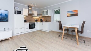 A modern kitchen with white cabinets, a microwave, and a coffee machine. There is a dining area with a table and chairs. - Vacation apartment 14 - Haus Seeperle (Esens)