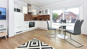 A modern kitchen with white cabinets, a wooden countertop, and a dining area with a round table and two chairs. - Vacation apartment 18 - Haus Seeperle (Esens)