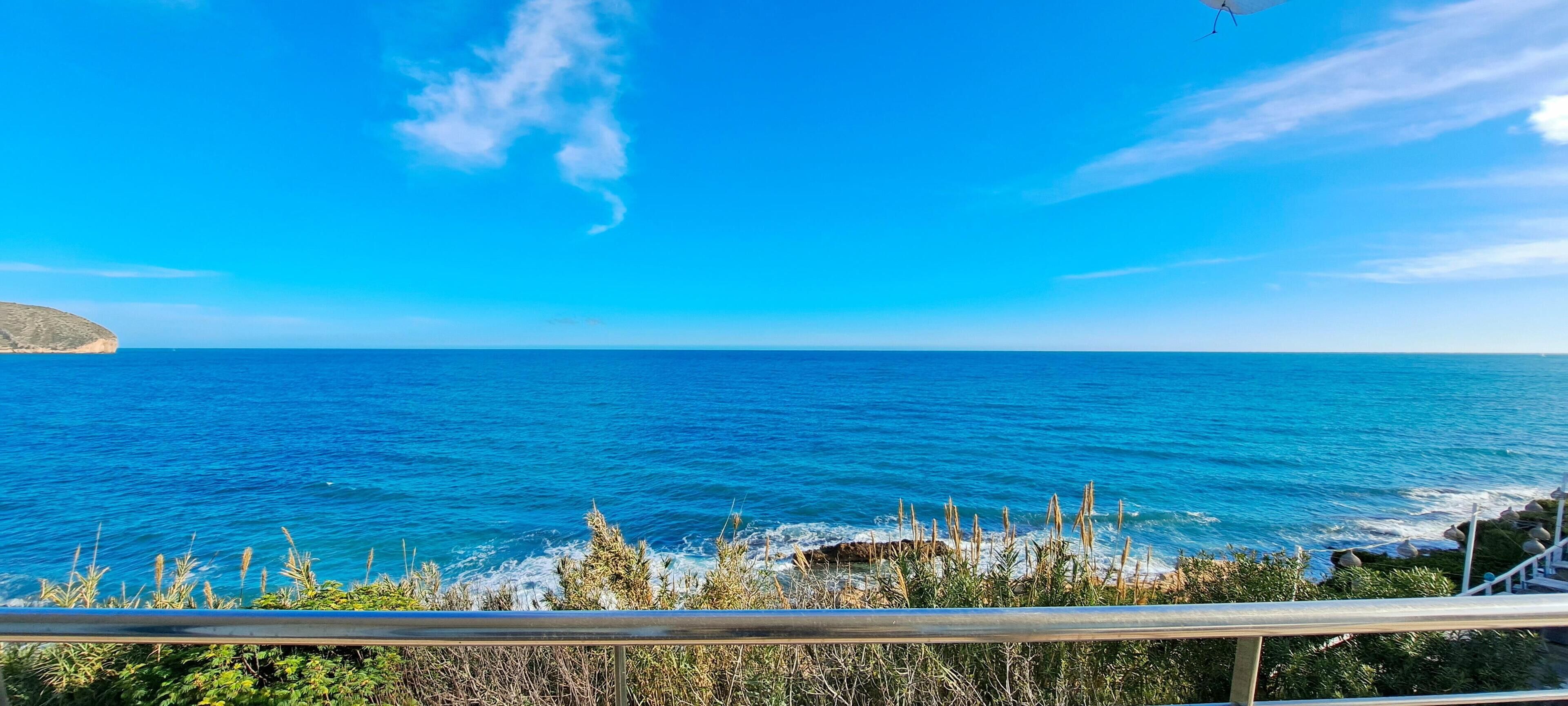 A coastal view with a clear sky, a rocky shoreline, and a distant landmass.
