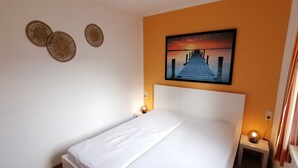 A bedroom with a bed, a painting of a pier, and two wall-mounted decorative items. - Beautiful bungalow near the Baltic Sea, family-friendly and quiet (Nienhagen)