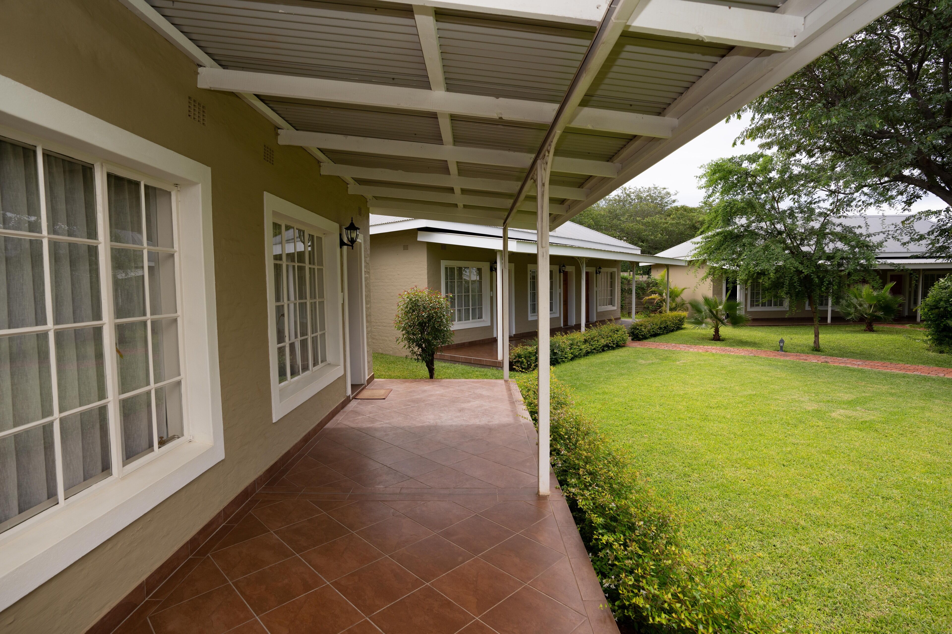 A covered porch with a tiled floor, a small tree, and a well-maintained lawn.