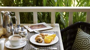 A table set with a cup of coffee, croissants, and orange slices on a placemat, with a silver pitcher and a teapot on the table.