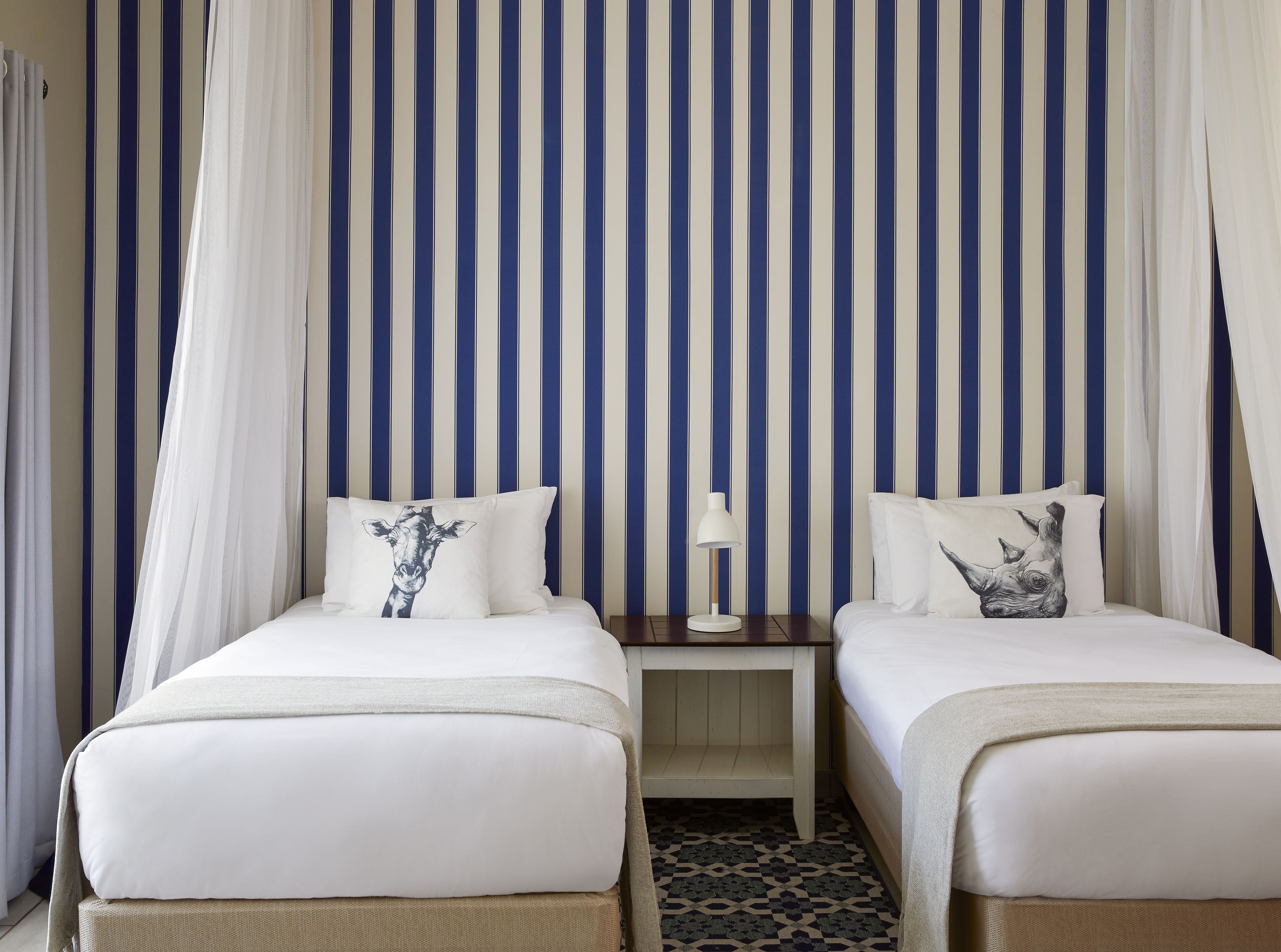 A hotel room with two beds, a nightstand, and a lamp.
