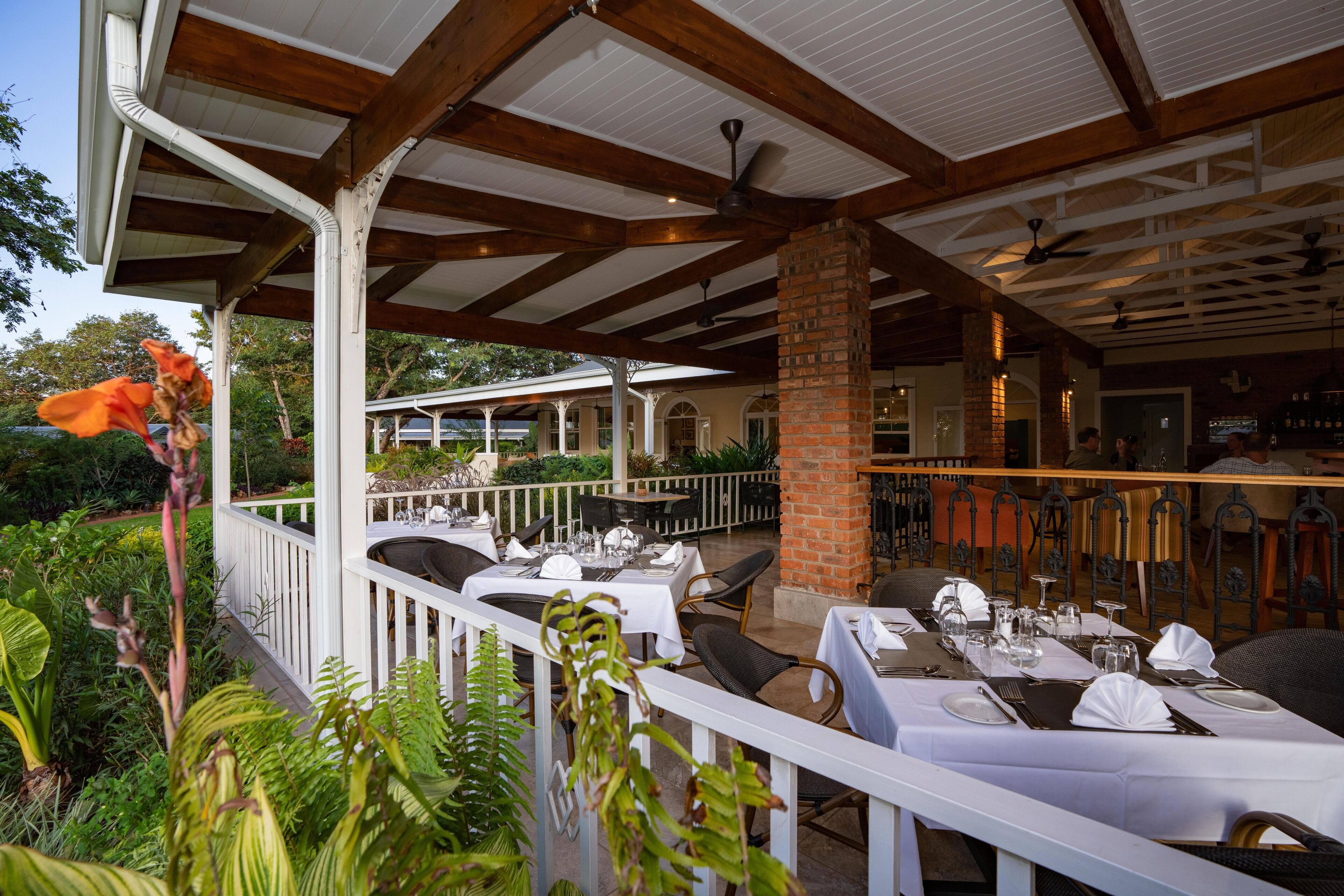 An outdoor dining area with white tables and chairs, brick pillars, and ceiling fans.