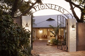 A gated entrance with a sign reading "PIONEERS" and a brick pathway leading to a building with a sloped roof. - Pioneers Lodge (Victoria Falls)