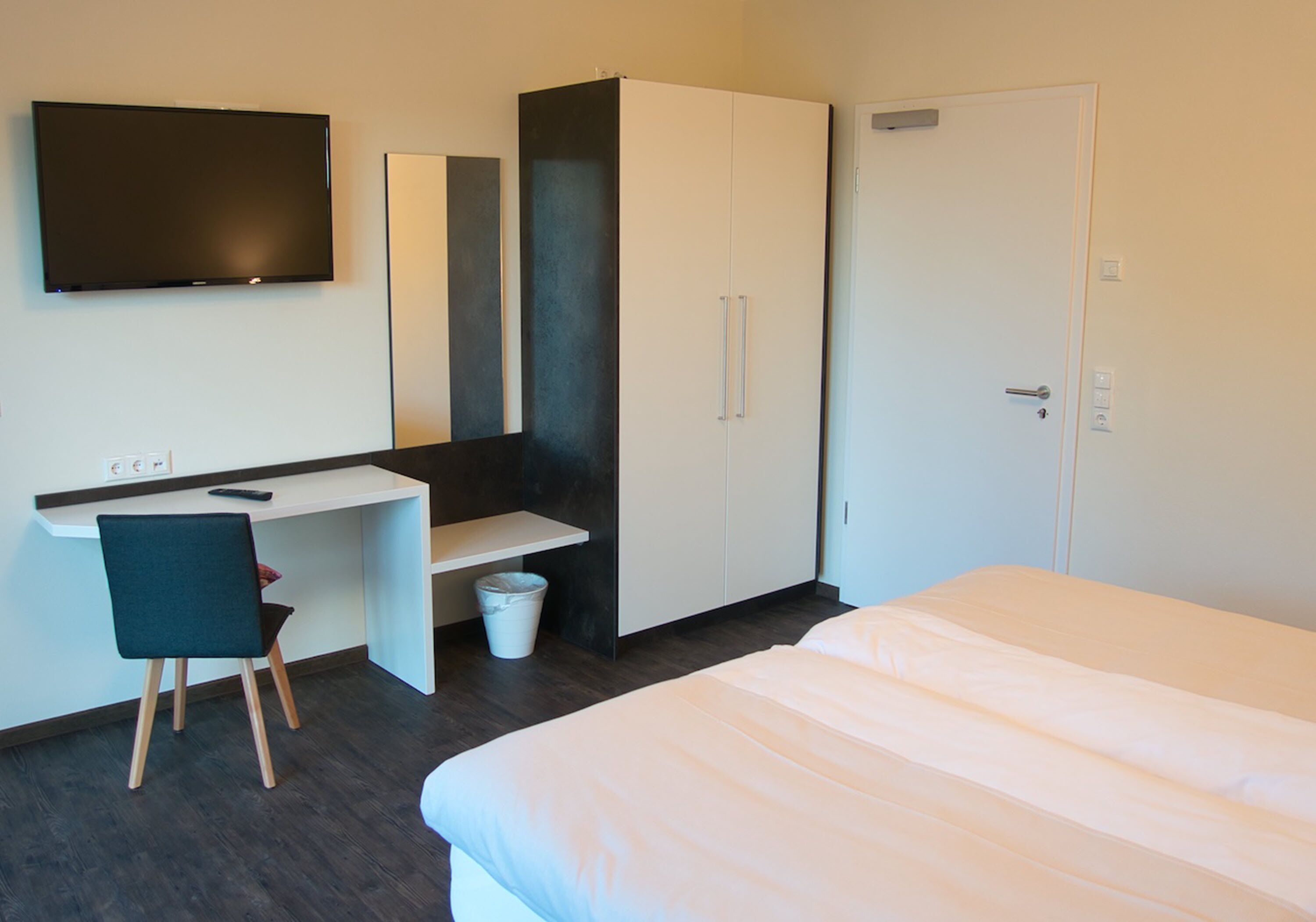 Habitación de hotel con cama, escritorio, silla, armario y televisión.