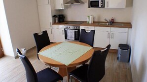 A compact kitchen with white cabinets, a microwave, a stove, and a sink. There is a round table with four chairs. - Hof Hahnenberg (Wagenfeld)