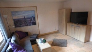 Ein stilvolles Wohnzimmer mit Sofa, Couchtisch, Fernseher und einem Gemälde an der Wand.