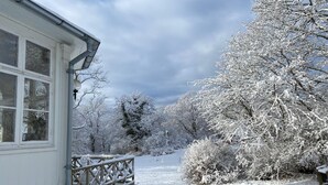 Un paysage enneigé avec une maison dotée de fondations en pierre, d’une terrasse en bois et d’une fenêtre à cadre blanc.