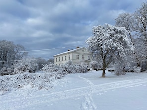 A large, white, two-story house with a symmetrical facade, surrounded by snow-covered trees and a snow-covered lawn. - Amiralsgården Werstorp (Nättraby)