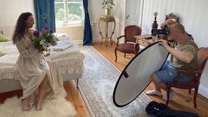 Une pièce avec un lit, une table sur laquelle se trouve une plante, une chaise et une personne tenant un appareil photo.