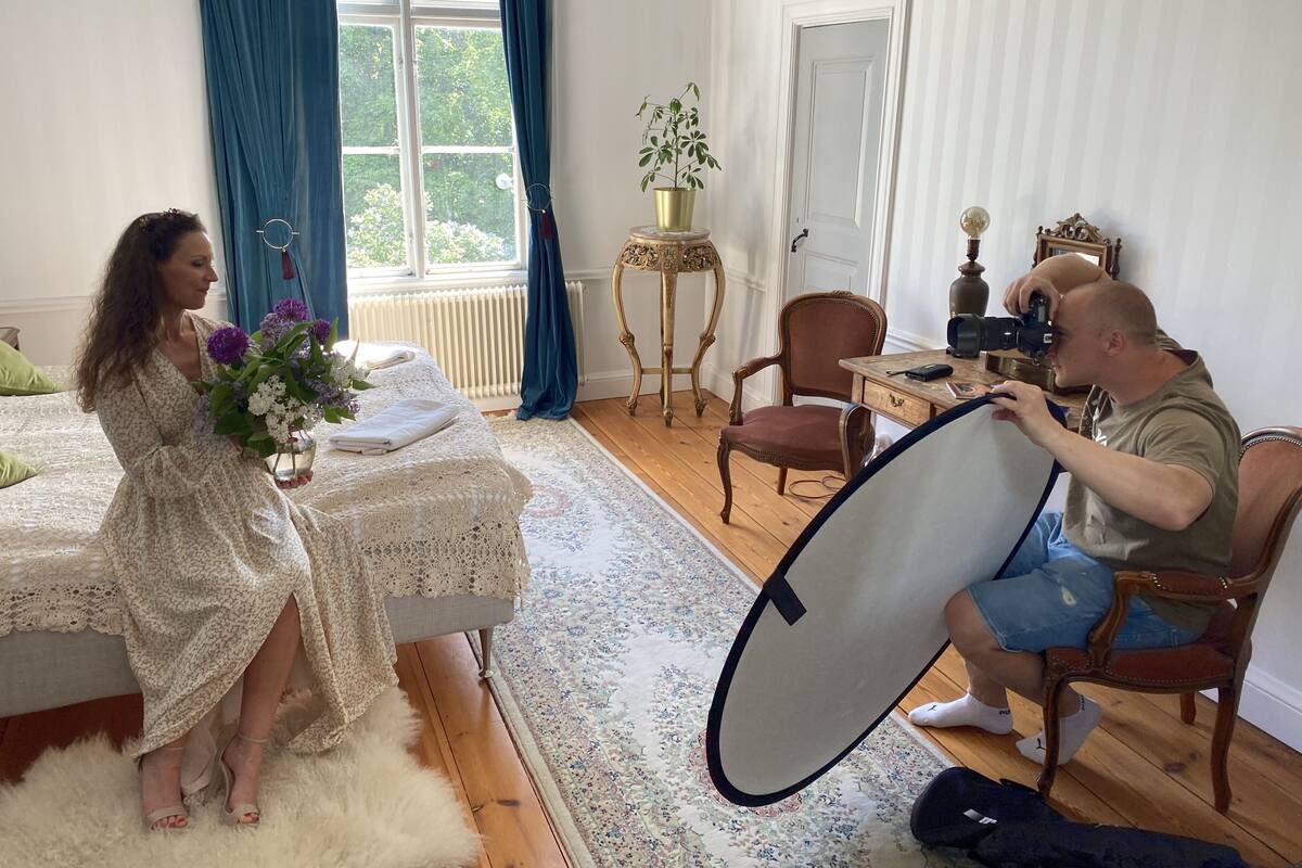 A room with a bed, a table with a plant, a chair, and a person holding a camera.