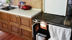 A kitchen with wooden cabinets, a tiled backsplash, a stove, and an oven. - Mountain style apartment (Zortea)