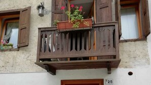 A white car parked in front of a building with a balcony, a red mailbox, and a door marked with the number 25. - Mountain style apartment (Zortea)
