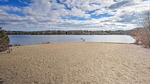 Una playa con un lago, árboles y un cielo nublado.