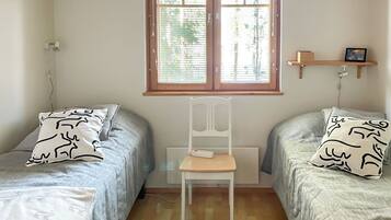 A room with two single beds, a chair, a window with blinds, a shelf with a picture, and a radiator.