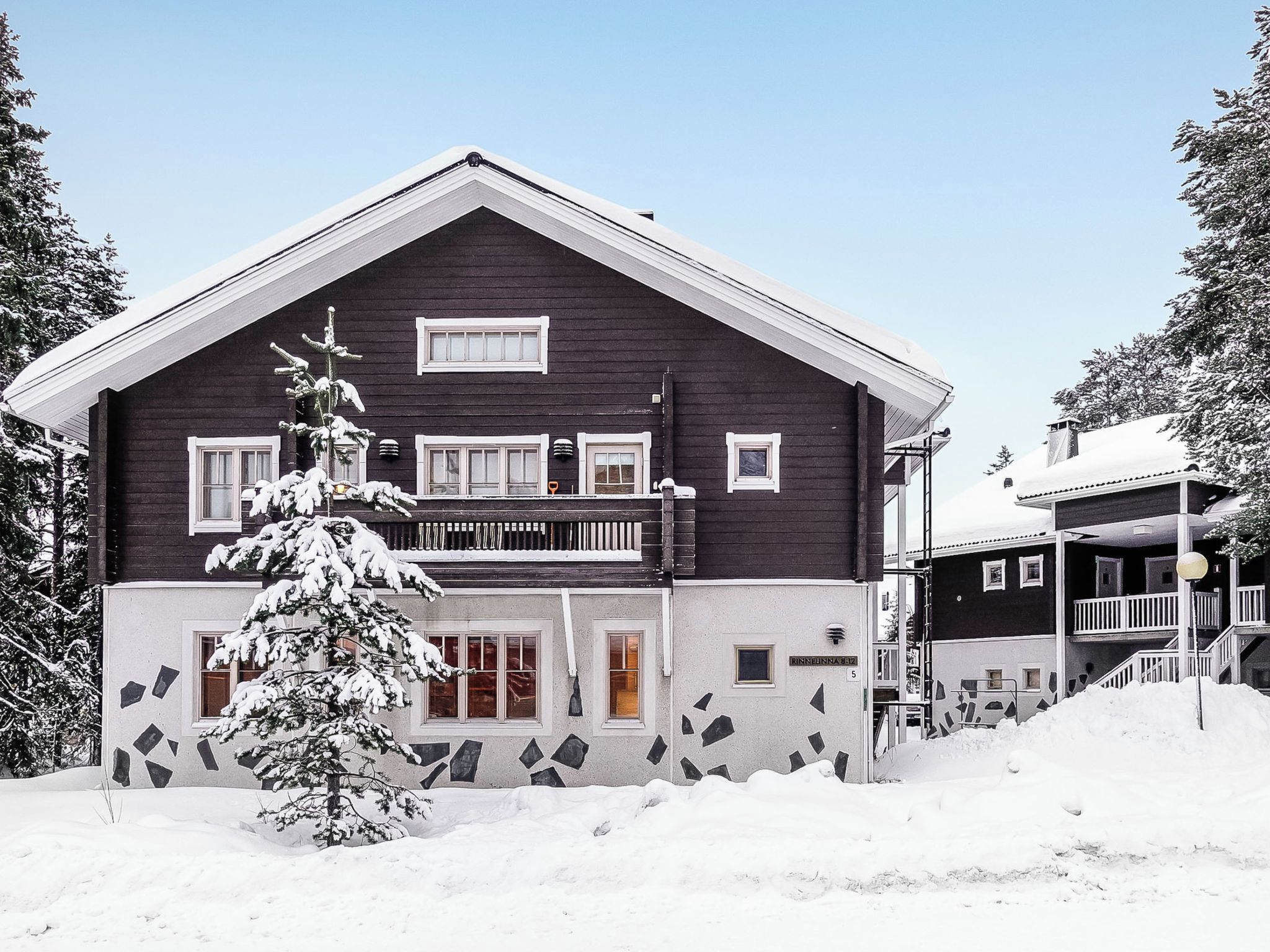 Kaksikerroksinen rakennus, jossa on tumma julkisivu, useita ikkunoita ja parveke.