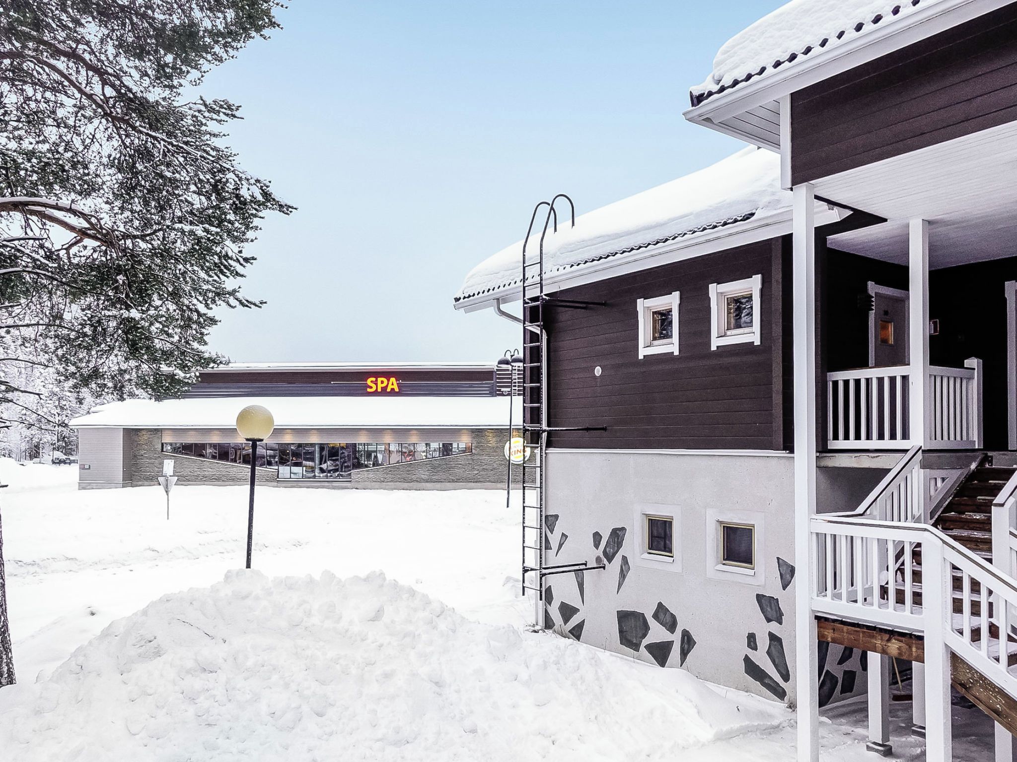 Een gebouw met twee verdiepingen, een balkon en een overdekte ingang, omringd door sneeuw.