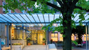 Ein Hotel mit Eingangsbereich, einer überdachten Laube, Treppen zum Eingang und einem Sitzbereich im Freien.