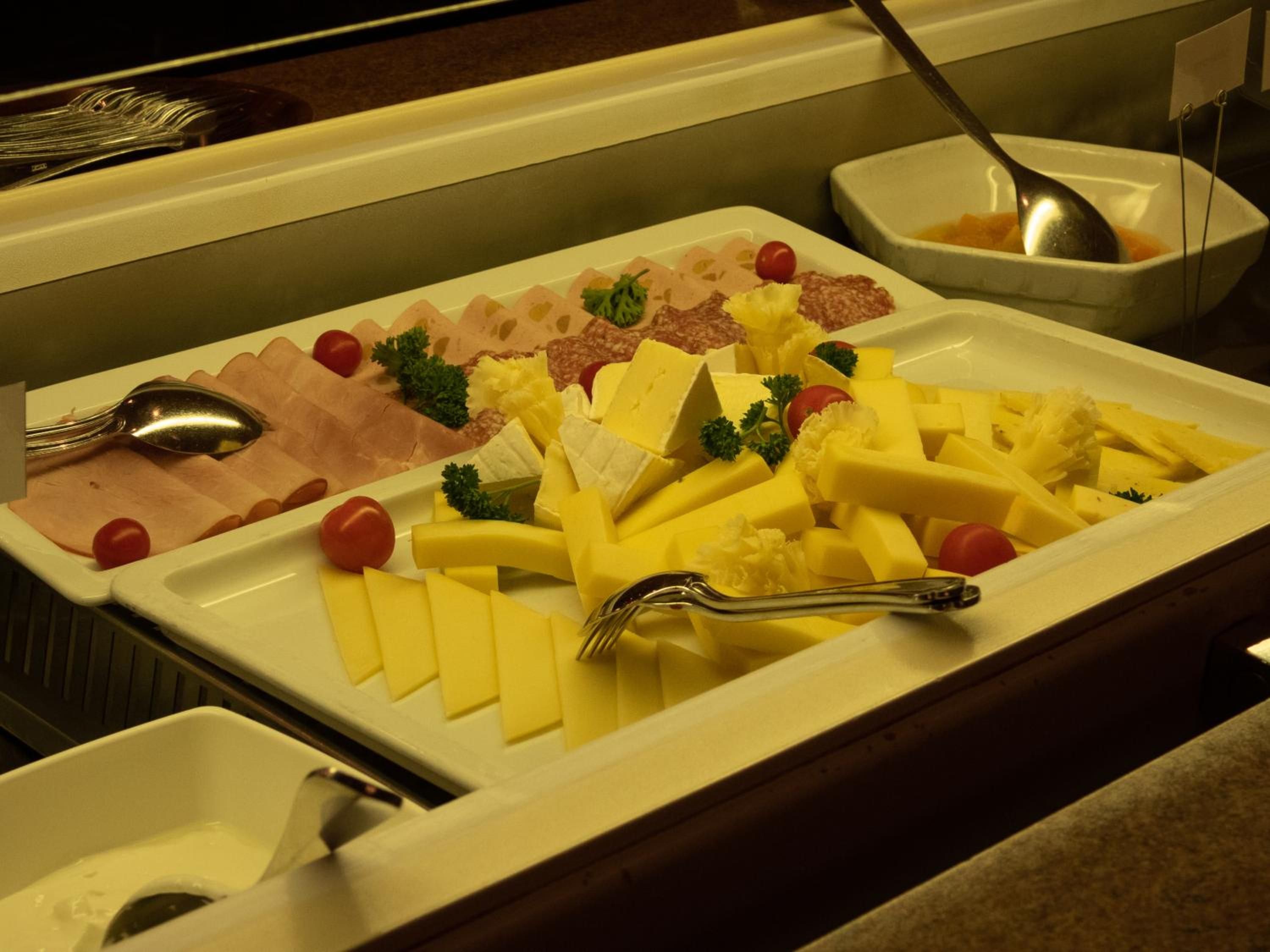 Un bufé con diversos quesos, carnes y guarniciones.