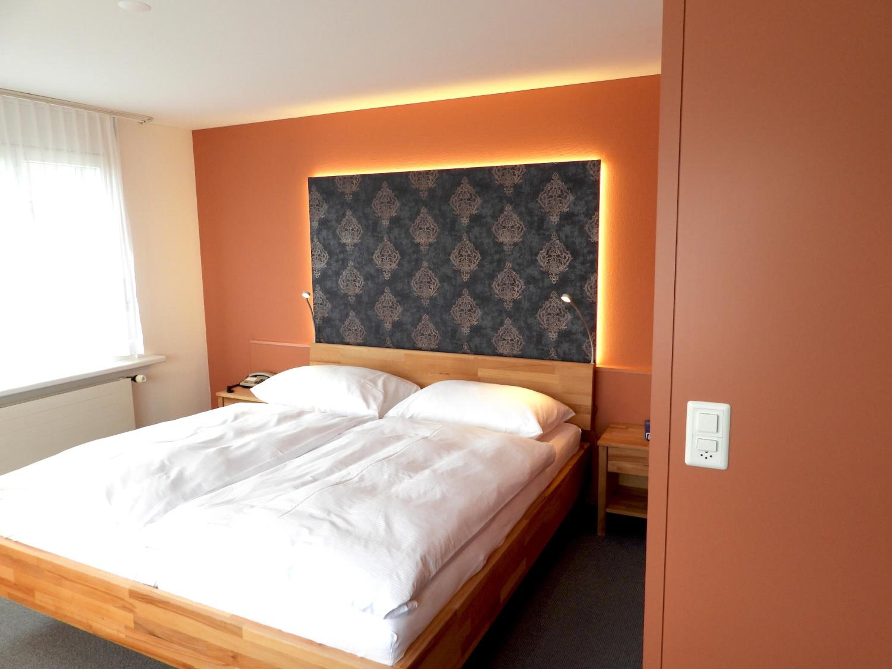 A neatly made bed with white linens in a room with a wooden headboard and a patterned wall.