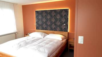 A neatly made bed with white linens in a room with a wooden headboard and a patterned wall.