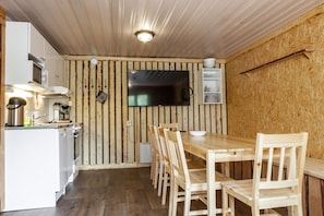 A compact kitchen with a wooden wall, a flat-screen TV, and a dining area with wooden chairs and a table.