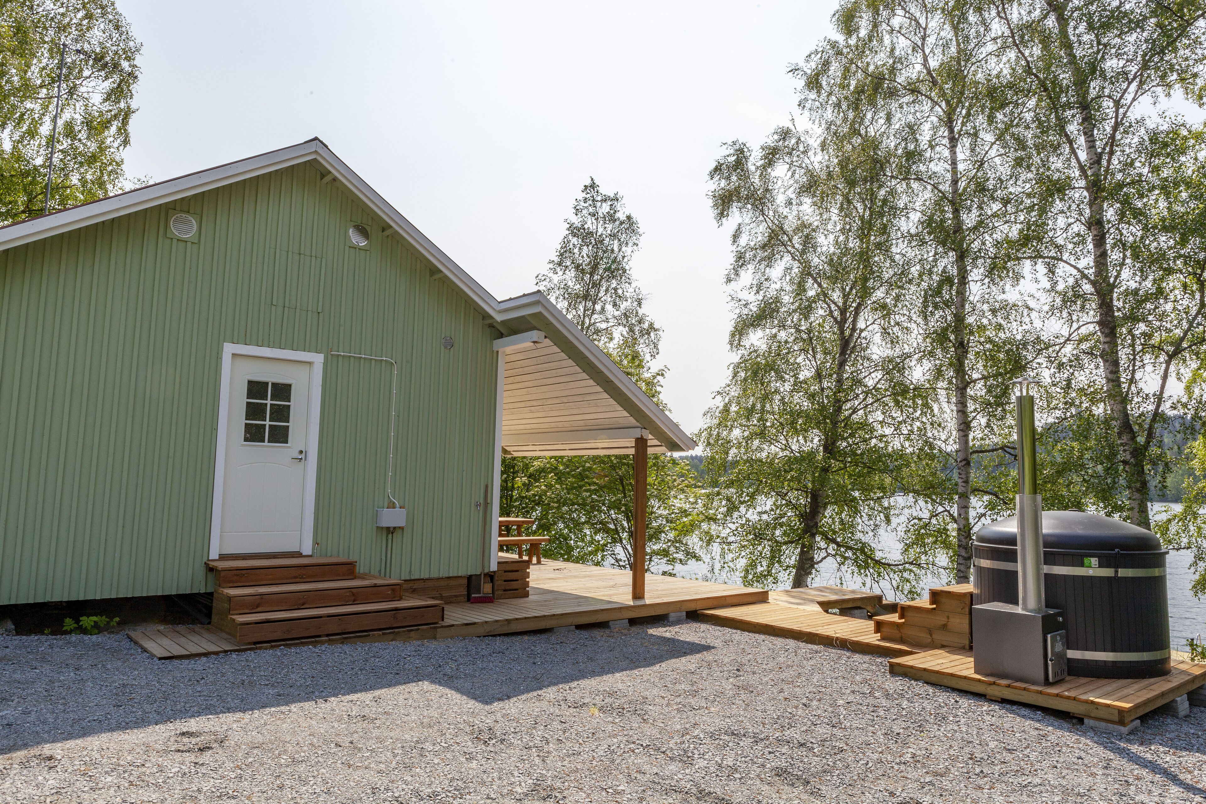 Een groen gebouw met een witte deur, houten trappen, een overdekte patio en een sauna.