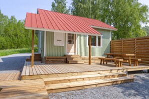 Una cabaña de madera pequeña con techo rojo, un porche con bancos y un camino de entrada de grava.