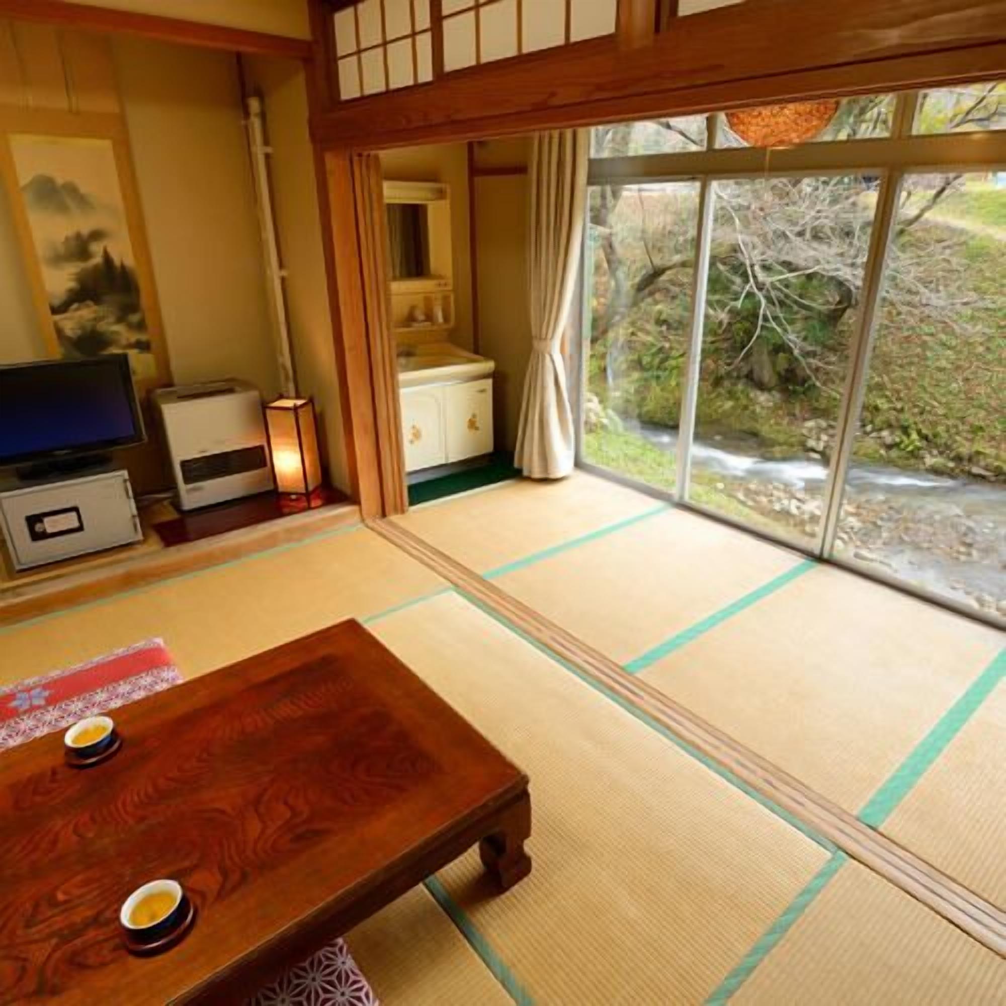 A tatami mat room with a wooden table, a television, and a view of a garden through a sliding door.