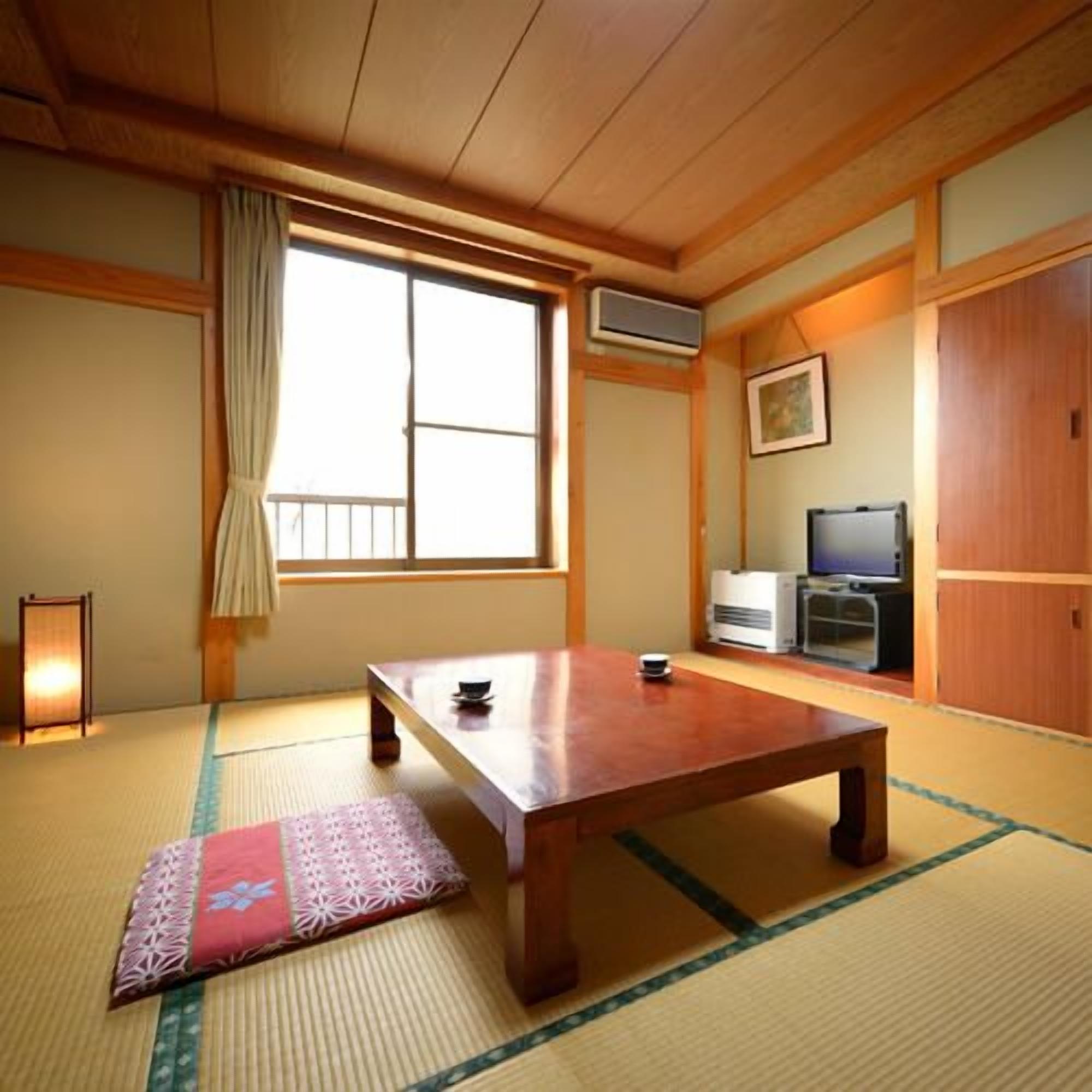 A traditional Japanese room with tatami flooring, a wooden table, a television, and a sliding door.