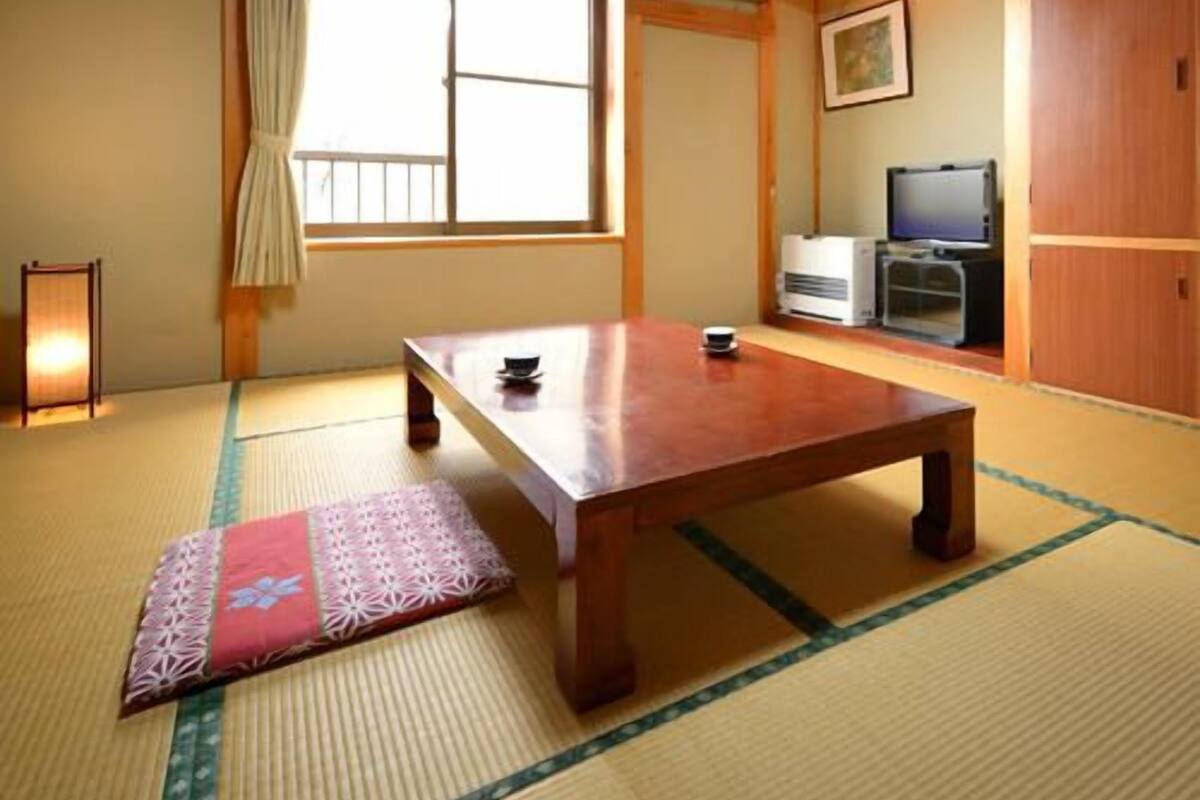 Um quarto japonês tradicional com tatames, uma mesa de madeira, uma televisão e uma porta deslizante.