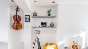 A room with a cello, a tripod, a yellow ottoman, shelves with decorative items, and a plant. - The Hollywood Beautiful 3 Bedroom House (Cardiff)