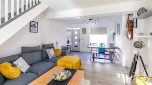 A modern living room with a grey sofa, yellow throw, and a wooden coffee table. A staircase with white railings leads to another room. - The Hollywood Beautiful 3 Bedroom House (Cardiff)