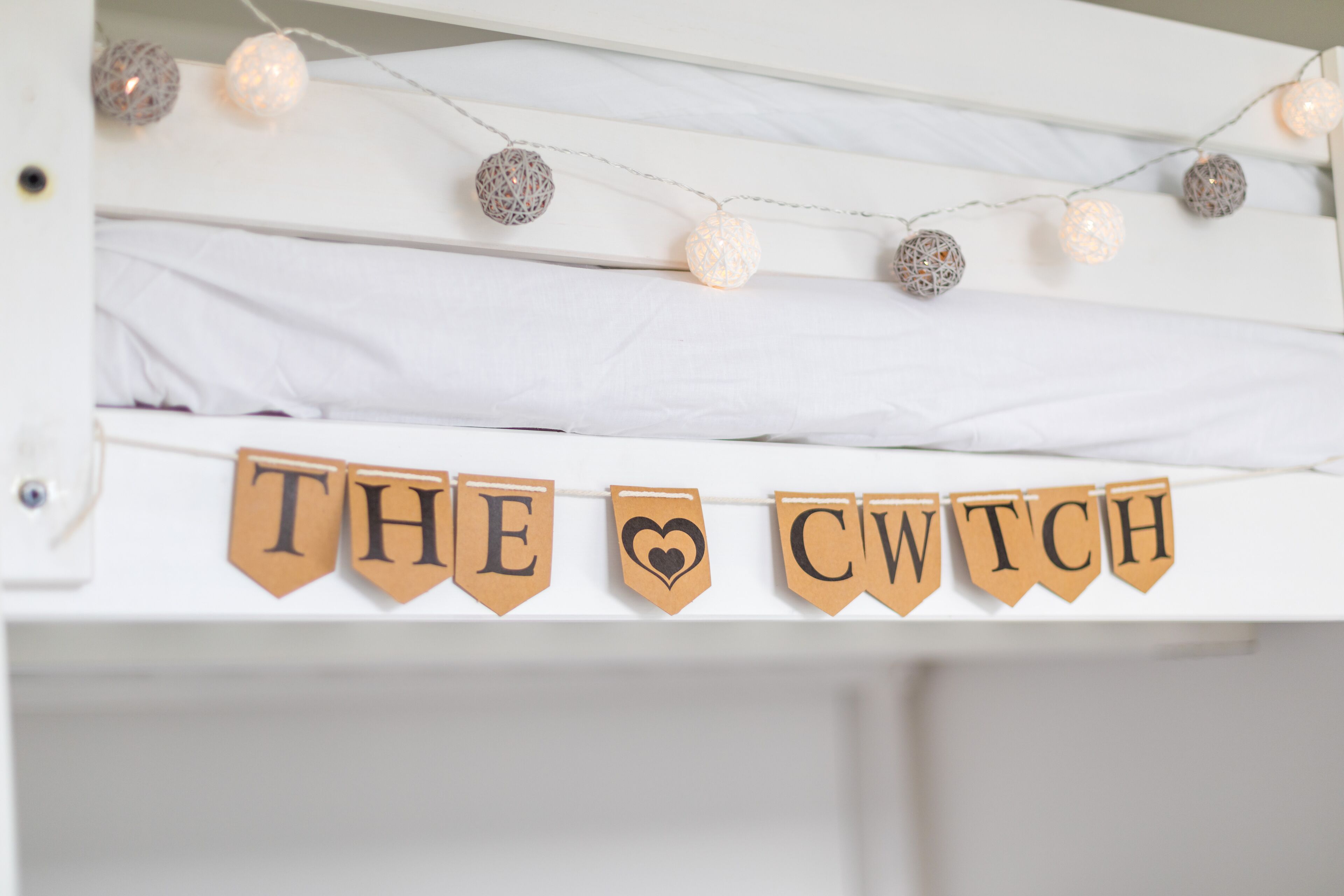 A bunk bed with a banner reading "THE CWTCH" and decorative string lights.