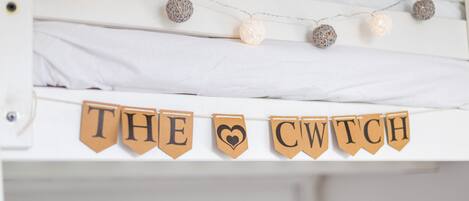 A bunk bed with a banner reading "THE CWTCH" and decorative string lights.