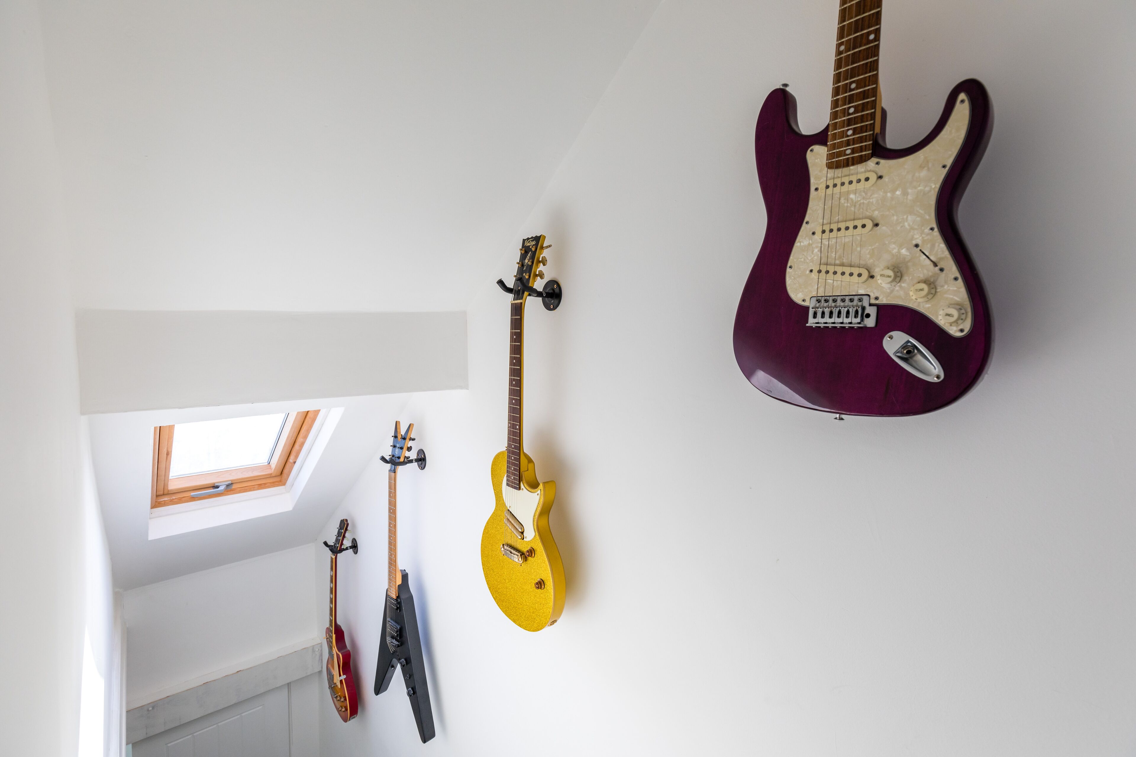 Ein Zimmer mit einem Oberlicht, einer Gitarre und einer violetten E-Gitarre, die an der Wand hängt.