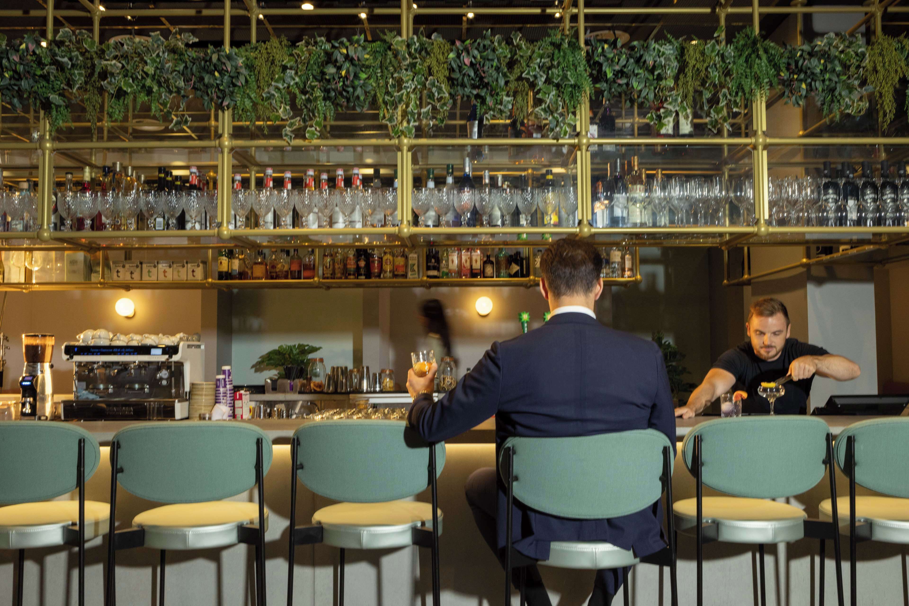 A bar area with multiple seating arrangements and a variety of bottles and glasses on shelves.