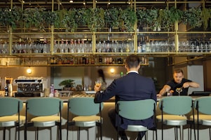 Zona bar con diversi tipi di sedute e varie bottiglie e bicchieri sugli scaffali.