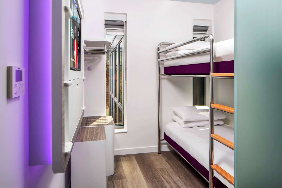 A compact hotel room with bunk beds, a small window, and a built-in wardrobe.