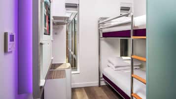 A compact hotel room with bunk beds, a small window, and a built-in wardrobe.